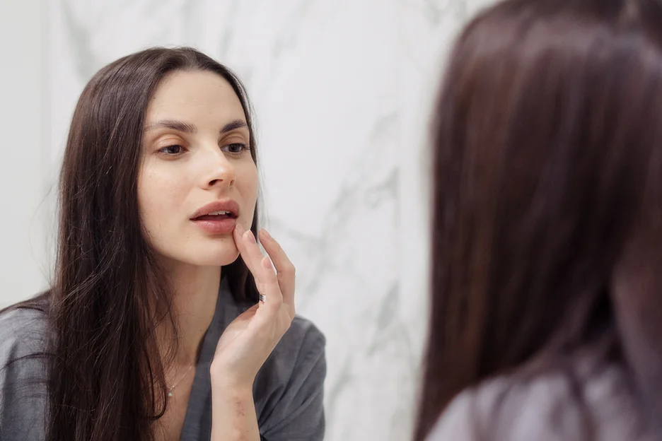 a woman checks her lips infront of the mirror while applying arnica after lip fillers