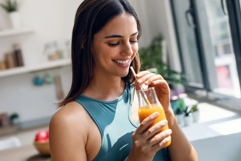 a woman uses straw while drinking her juice after lip fillers